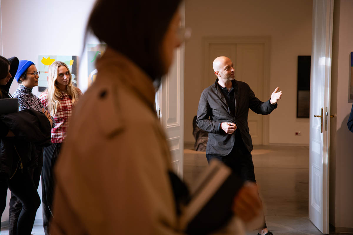 Prof. Prot Jarnuszkiewicz wyciągniętą dłonią wskazuje szczegół omawianej pracy uczestnikom wernisażu