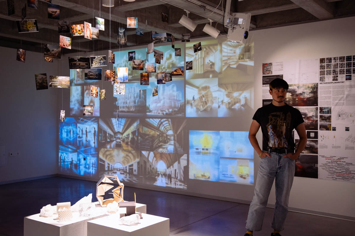 Mężczyzna w przestrzeni wystawowej na ścianach prezentowane zdjęcia, także wyświetlane z projektora. W środku sali zdjęcia na sznurkach zwisają z sufitu