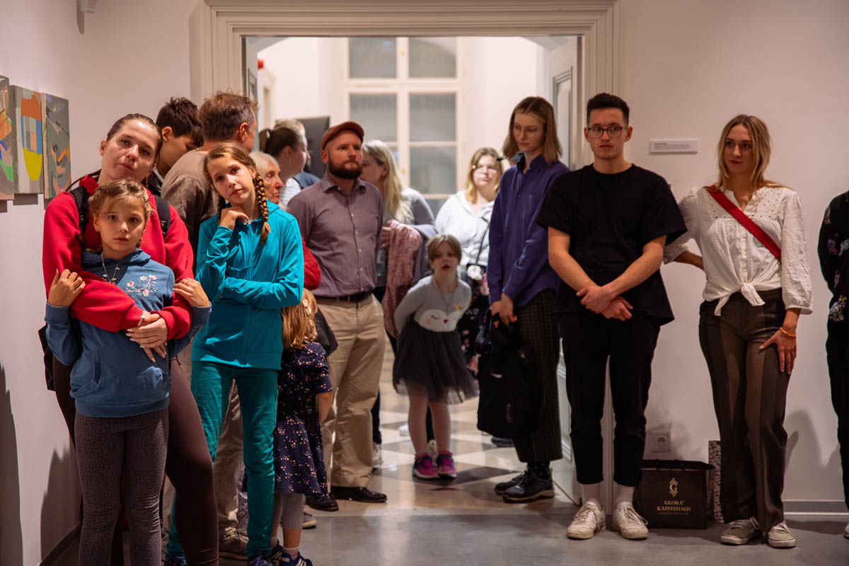 Grupa gości wernisażu. Pomiędzy dorosłymi stoją dzieci