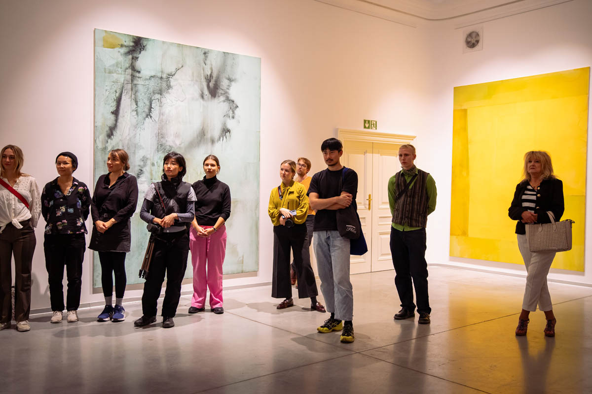Uczestnicy wernisażu w przestrzeni wystawowej, na ścianach są zawieszone wielkoformatowe grafiki
