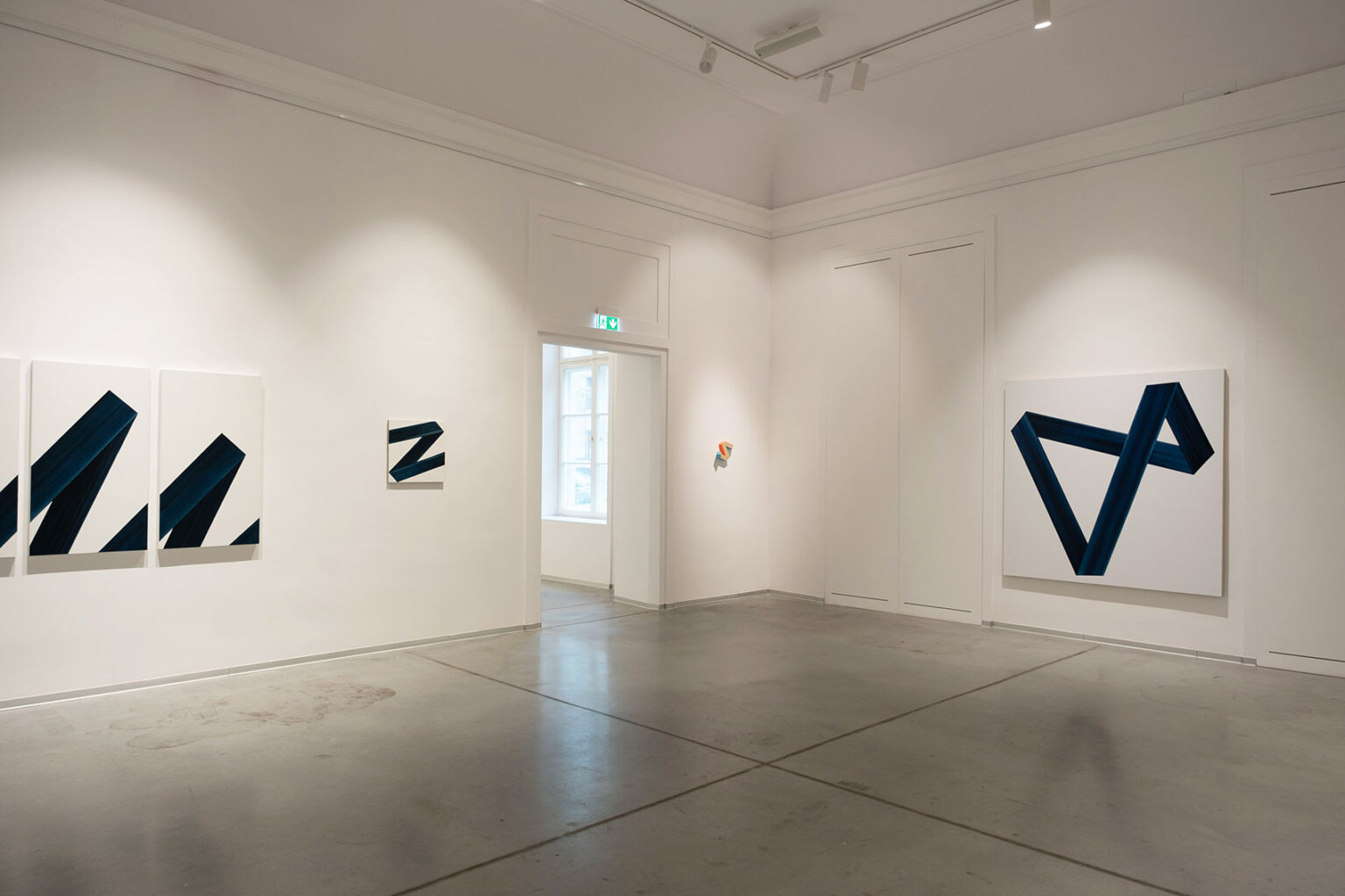 Kolorowe, geometryczne formy przestrzenne na ścianie galerii