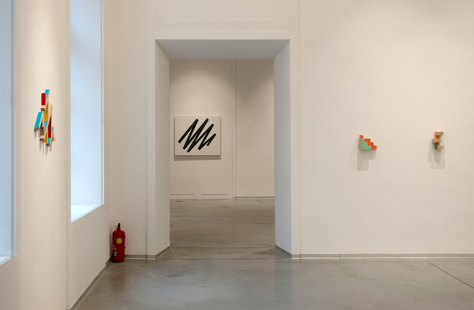 Kolorowe, geometryczne formy przestrzenne na ścianie galerii