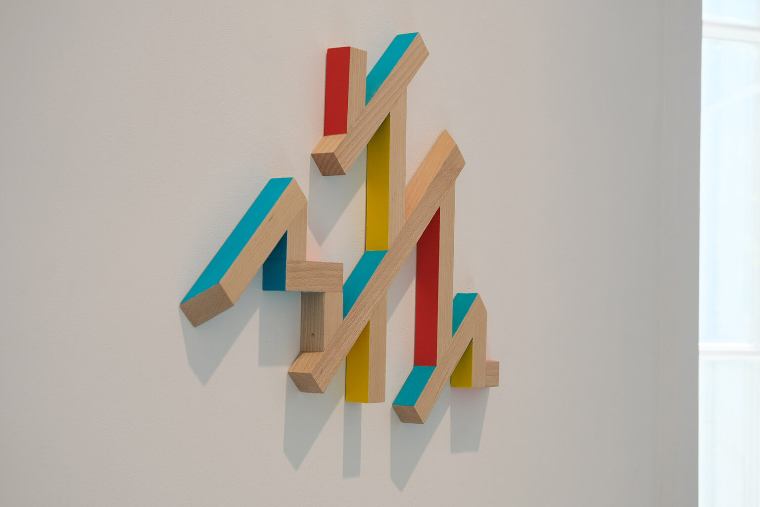 Kolorowe, geometryczne formy przestrzenne na ścianie galerii