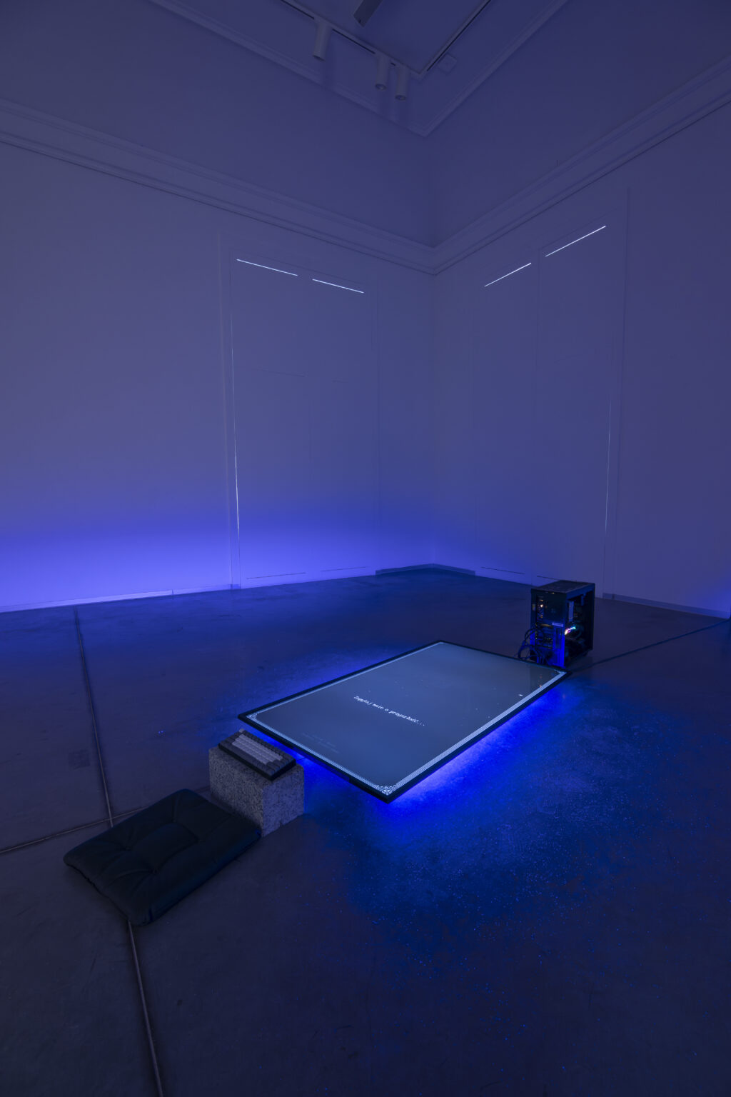 W wyciemnionej przestrzeni na podłodze leży duży płaski ekranem. Spod ekranu świeci niebieskie światło