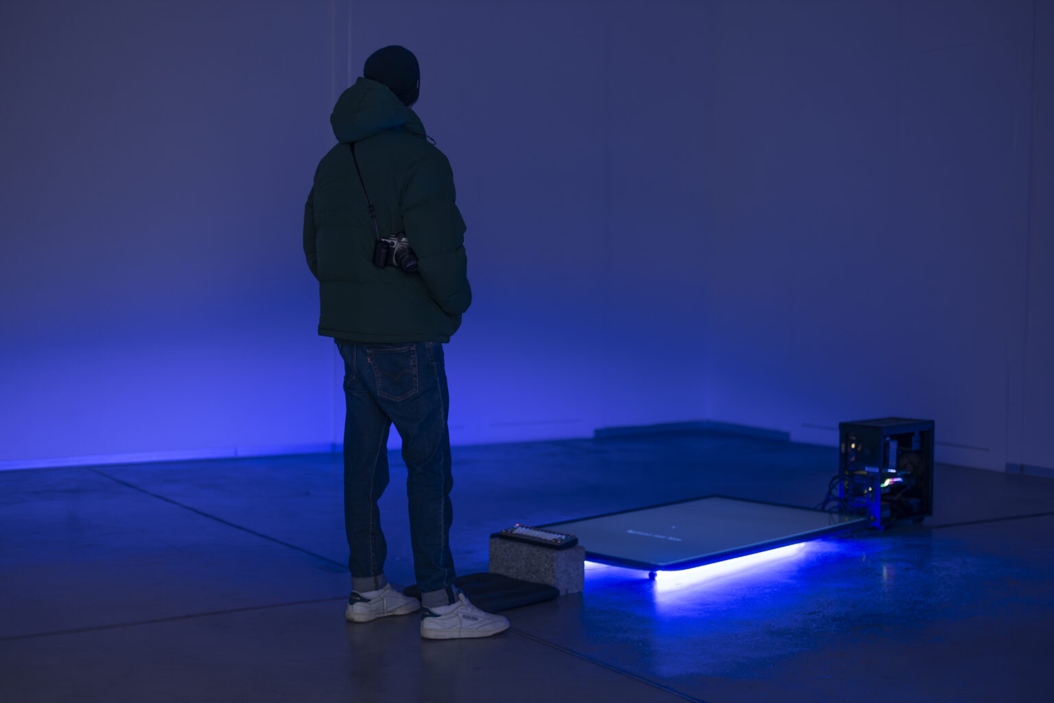 Mężczyzna stoi przed dużym płaskim ekranem leżącym na podłodze. Spod ekranu świeci niebieskie światło