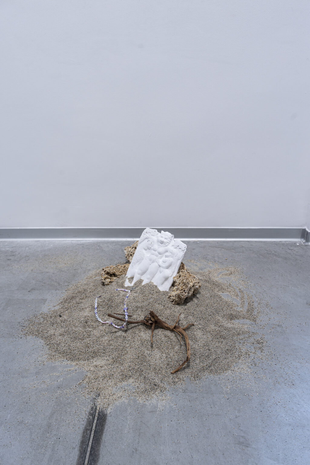 Gipsowa forma oraz różnokolorowe koraliki zakopana w górce z pisaku usypanej na podłodze