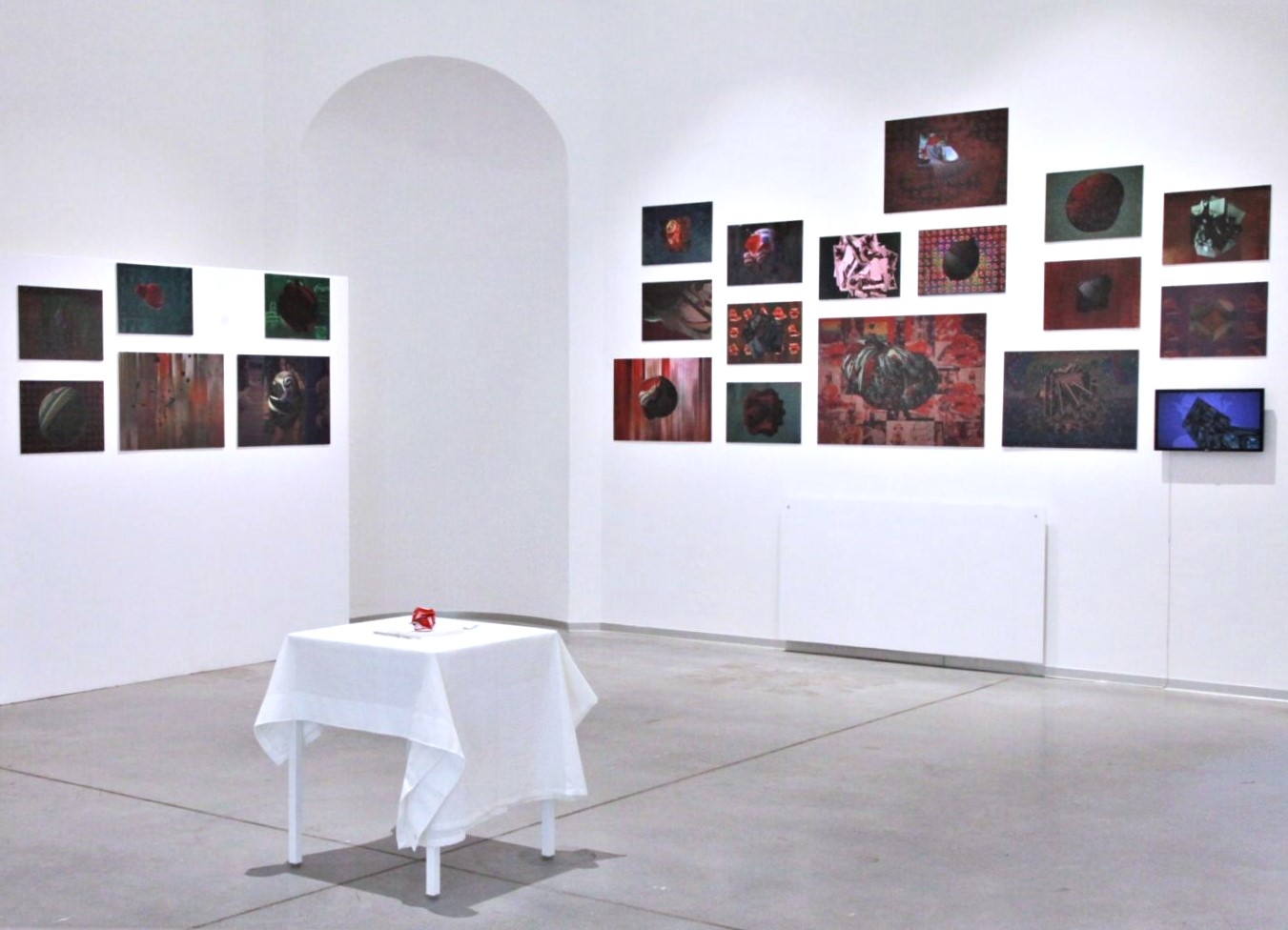 Po środku sali wystawowej nakryty białym obrusem stolik, na ścianach prezentowane są różnego rozmiaru obrazy