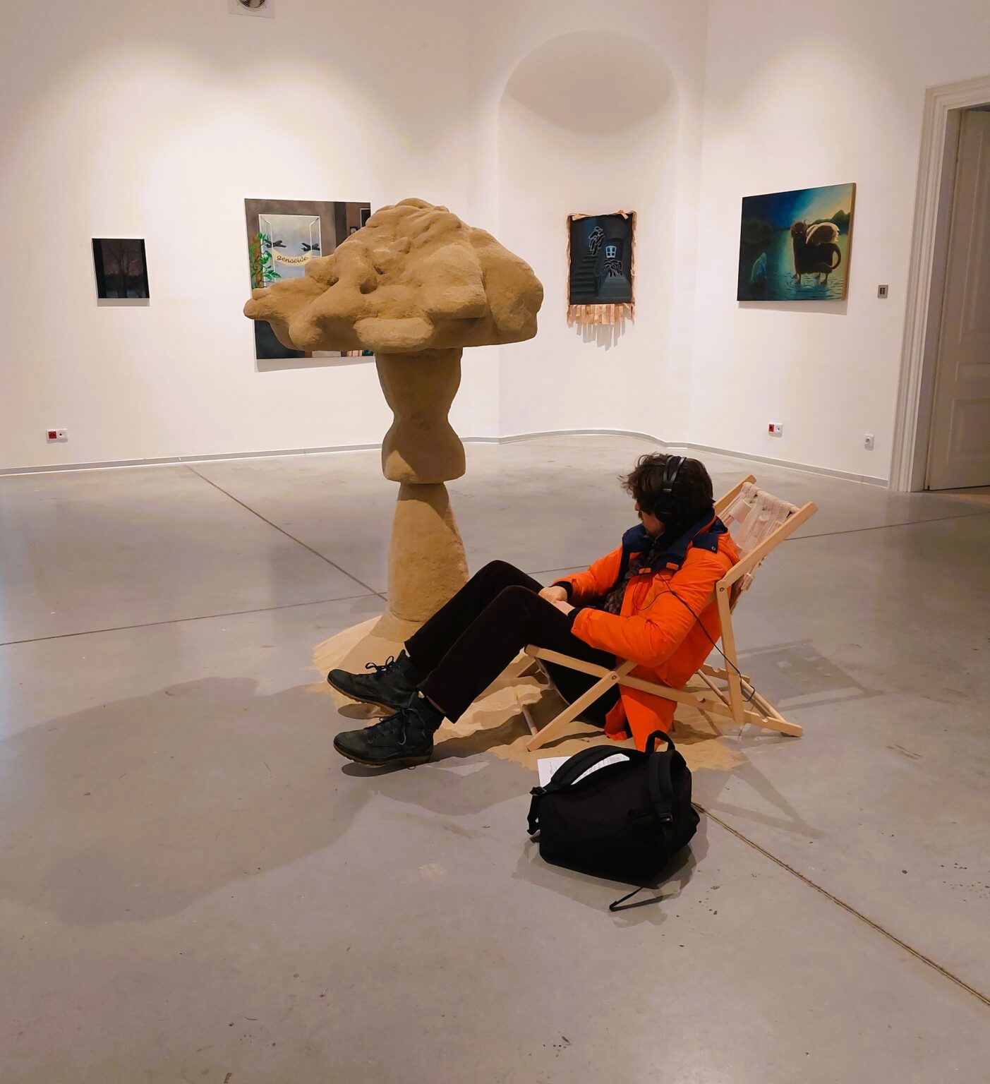 Kobieta siedząca na krześle. Obok stojąca forma przypominająca grzyba.