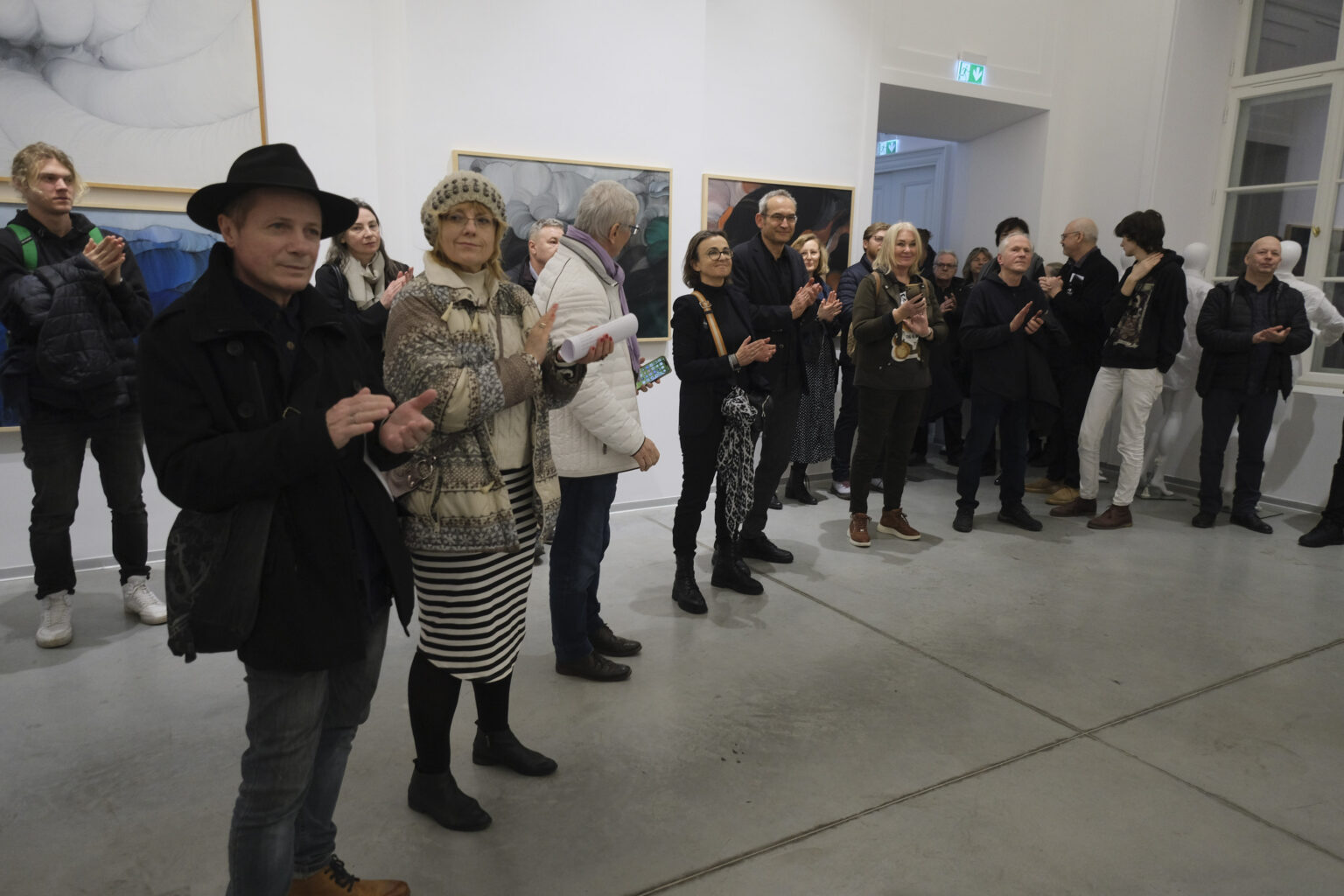 Widzowie wystawy stoją w większej grupie w przestrzeni galerii. Na ścianach wiszą obrazy Konrada Jarodzkiego.