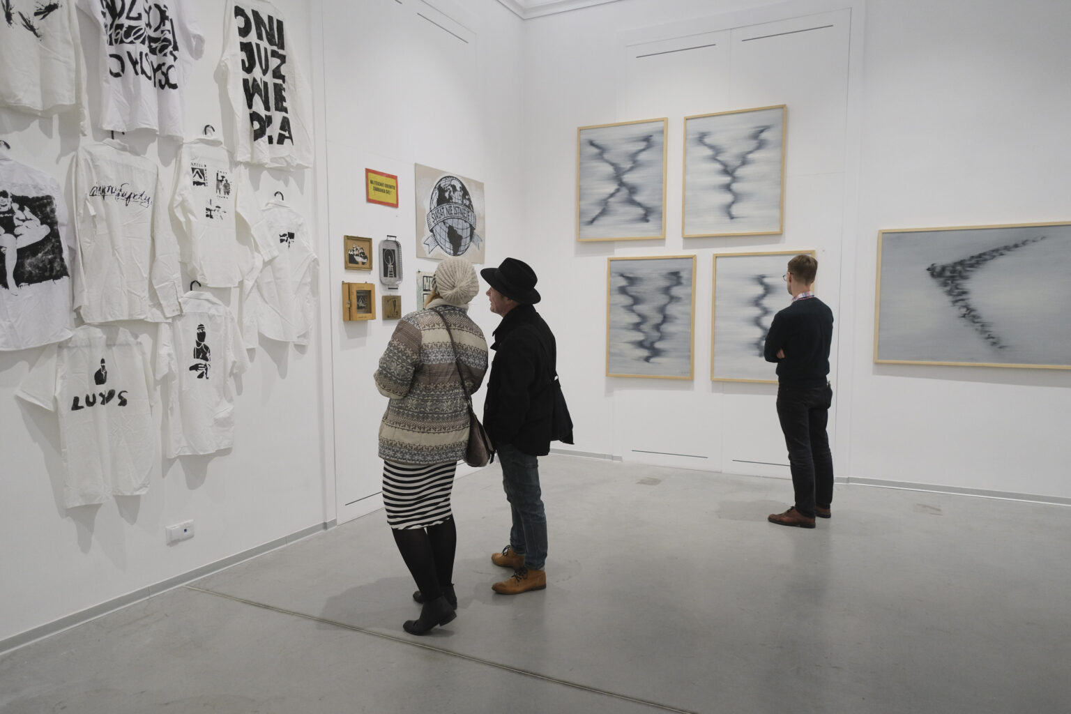 ytzy osoby w przestrzeni galerii oglądają prace Konrada i Pawła Jarodzkich zawieszone na ścianach.
