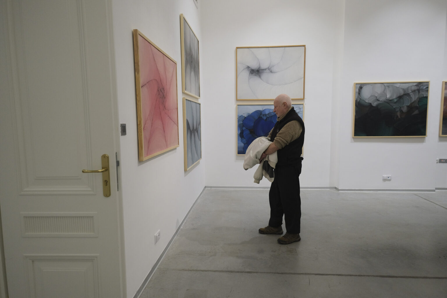 Mężczyzna ogląda prace malarskie Konrada Jarodzkiego wiszące na ścianach.