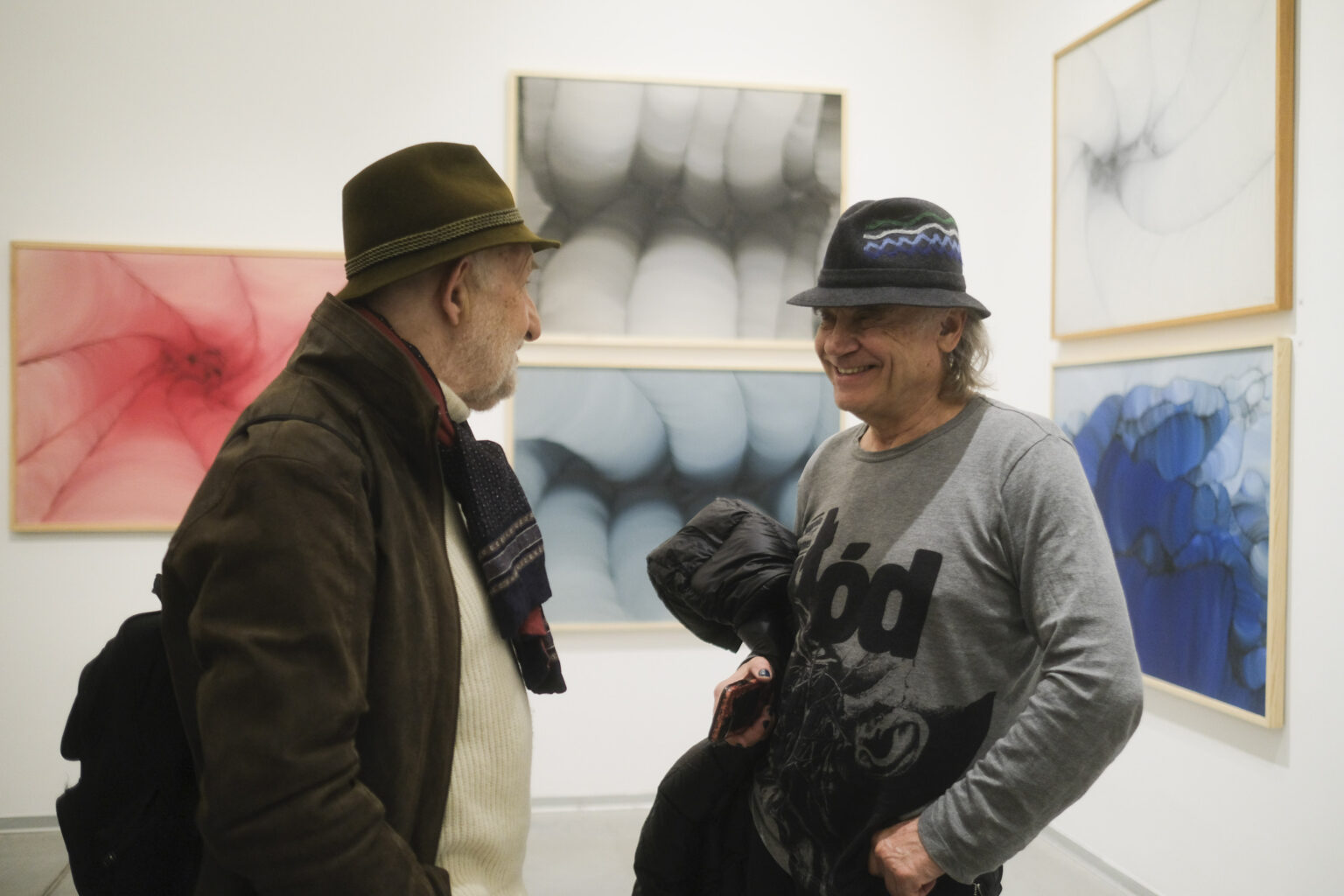 Dwóch panów rozmawia ze sobą na tle prac malarskich Konrada Jarodzkiego