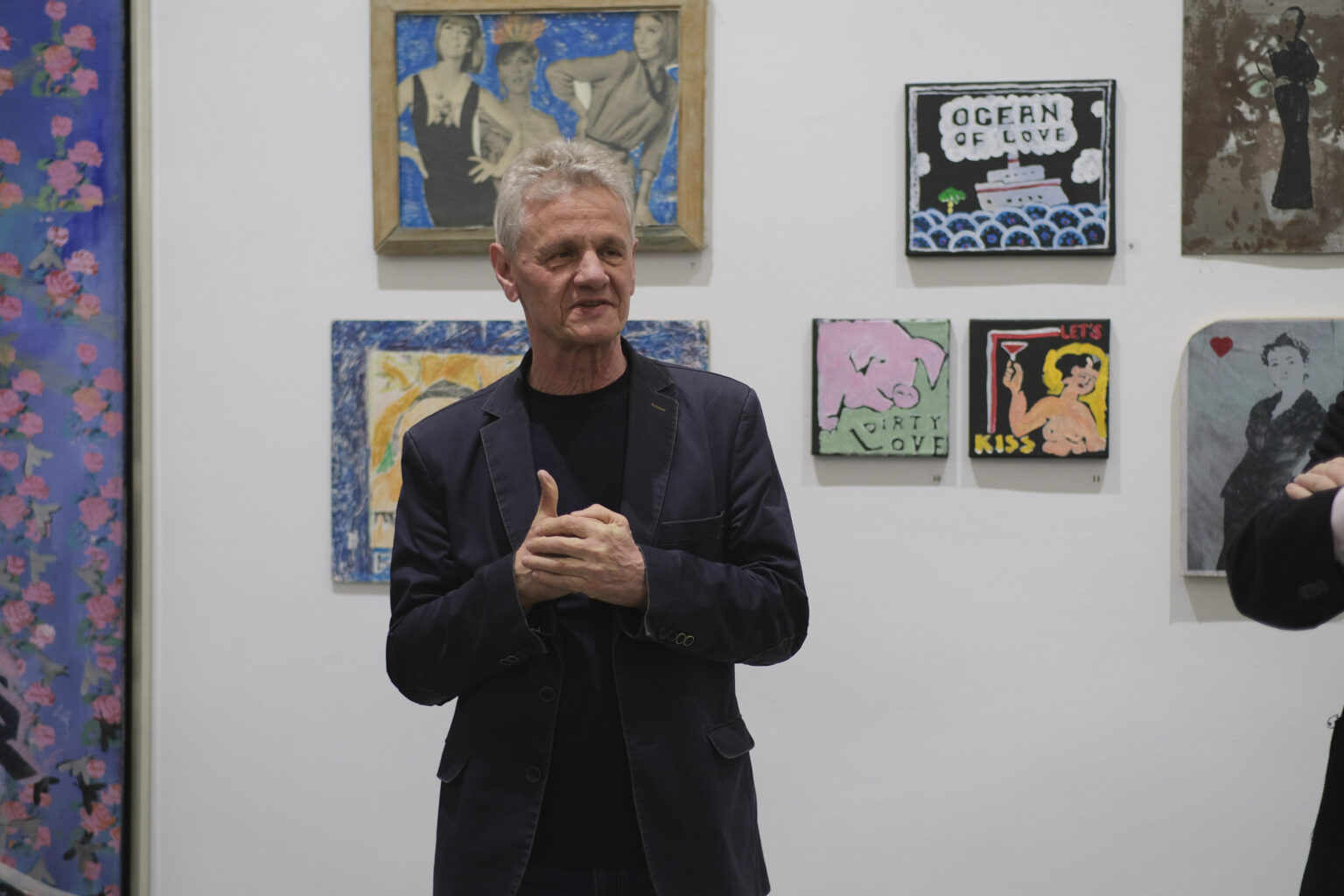 Kurator wystawy Marek Śnieciński stoi na tle obrazów Pawła Jarodzkiego.