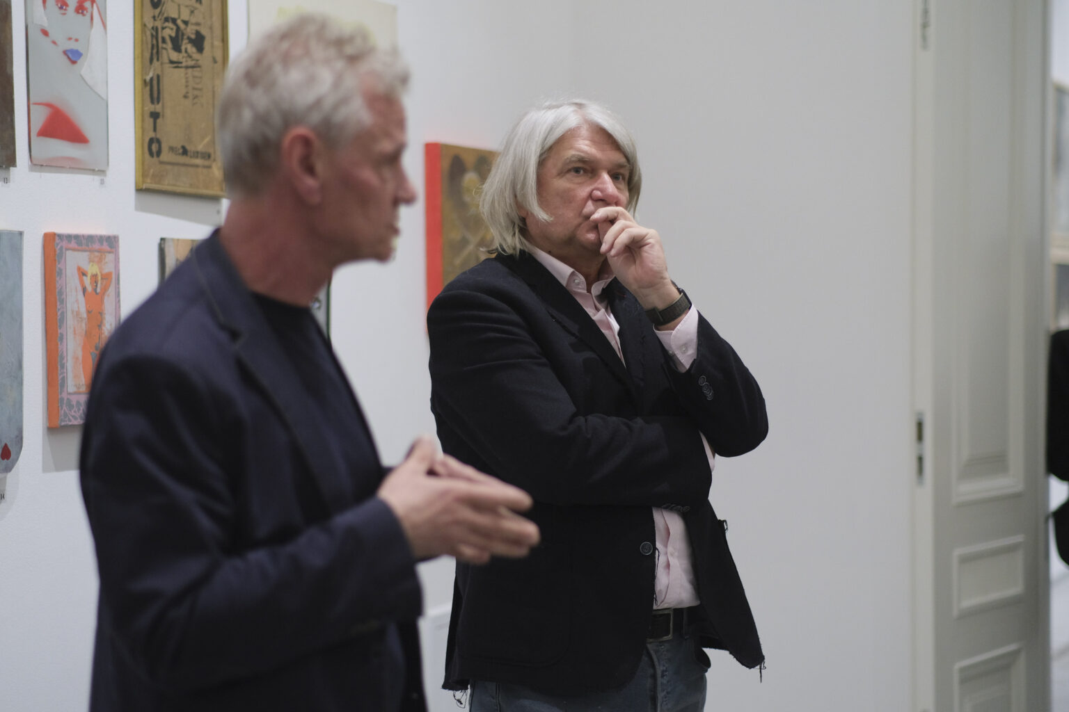 Dyrektor galerii prof. Paweł Nowak oraz kurator wystawy Marek Śnieciński stoją na tle obrazów Pawła Jarodzkiego.