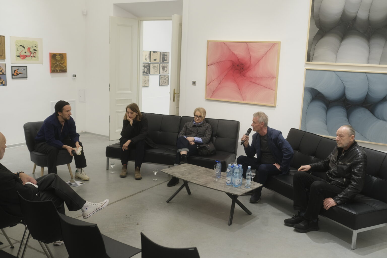 Na tle obrazów Konrada i Pawła Jarodzkich siedzą na czarnych kanapach prelegenci debaty.