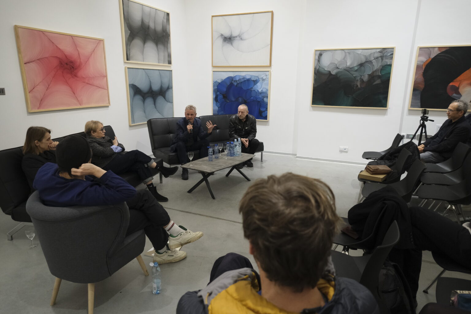 Na tle obrazów Konrada i Pawła Jarodzkich siedzą na czarnych kanapach prelegenci debaty.