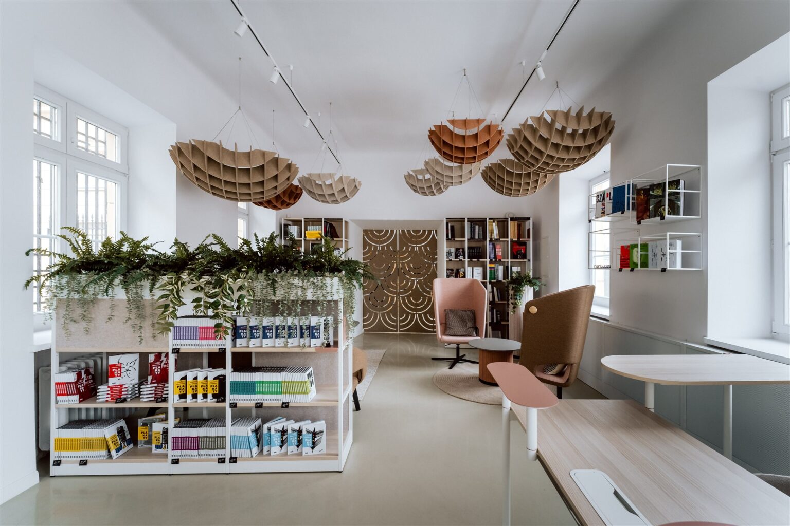 Nowocześnie umeblowane, jasne wnętrze z regałami na książki i podwieszonymi z sufitu kolistymi ozdobami