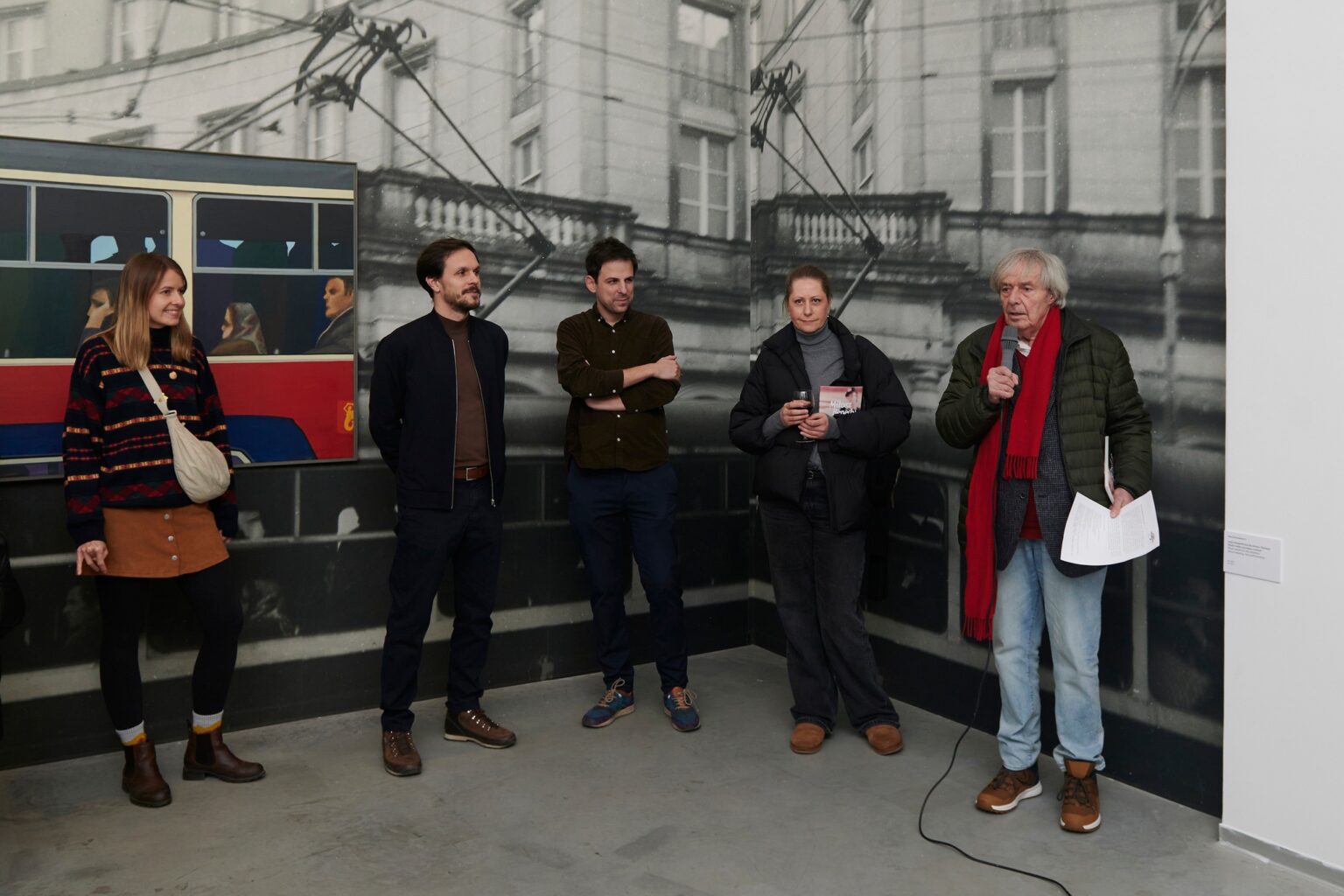 pięć osób stoi na tle fototapety z czarno-białym zdjęciem miasta i kolorowy obrazem przedstawiającym ludzi w czerwonym autobusie