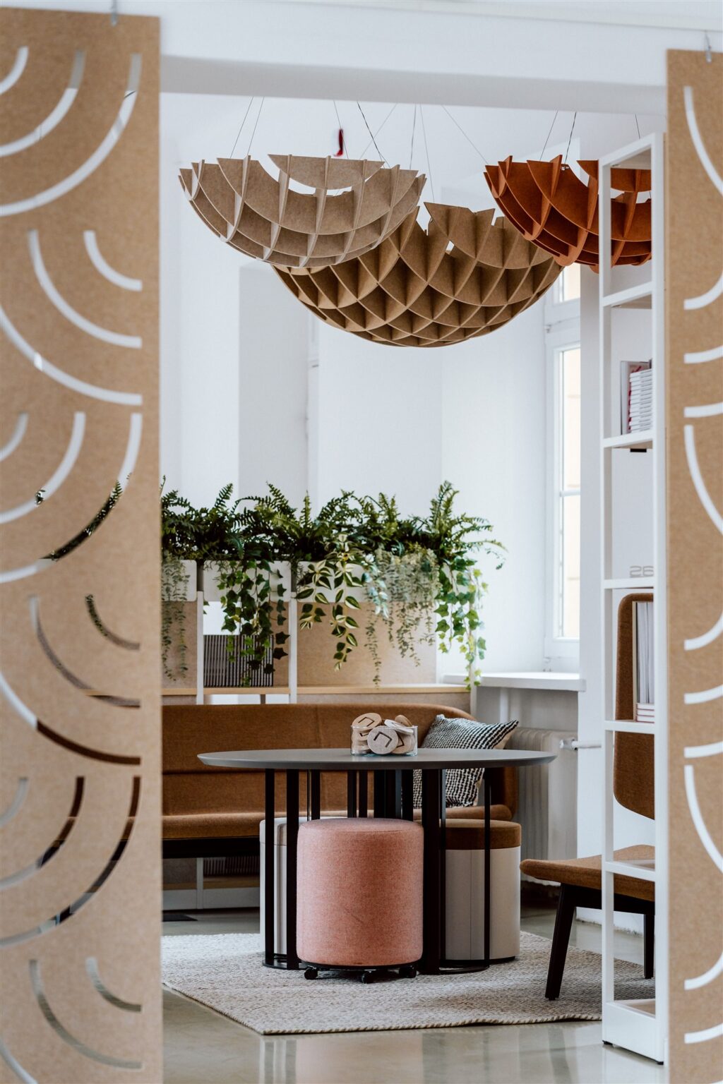 Widok jasnego pomieszczenia przez rozsunięte ozdobne przepierzenie, w tle siedziska, rosliny w doniczkach i podwieszone pod sufitem kuliste ozdoby