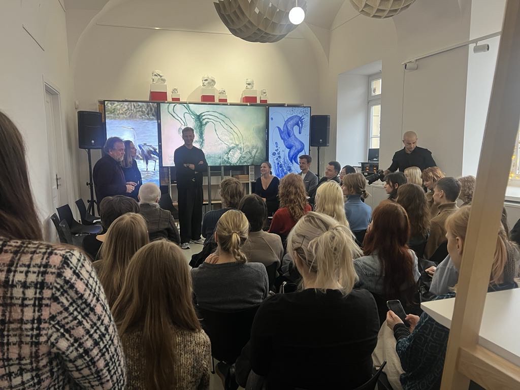 Publiczność obserwuje 3 duże ekrany wyświetlające kolorowe prace studentów