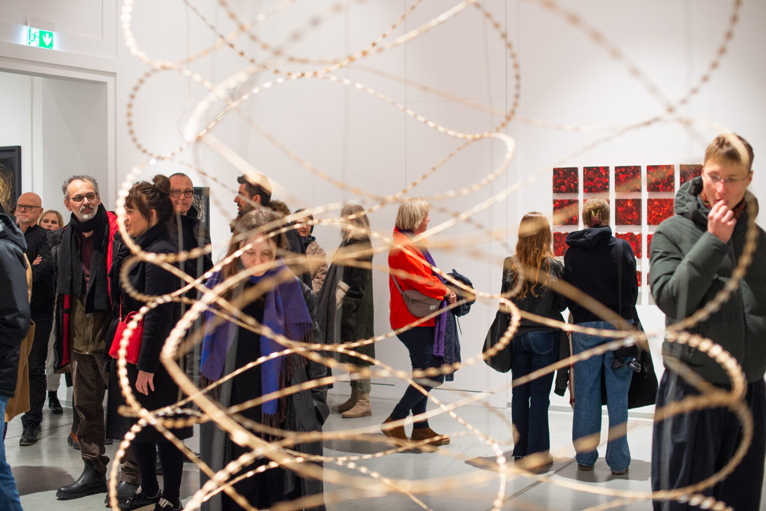 na pierwszym planie ażurowa instalacja, w tle grupa ludzi na tle wystawy