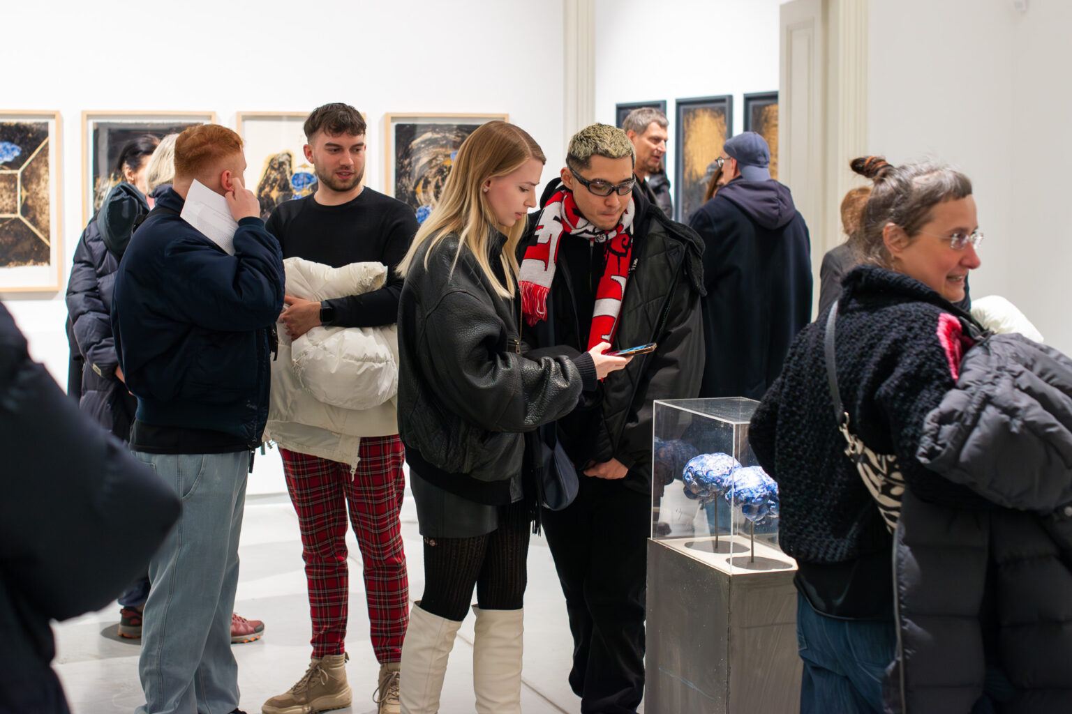 grupa osób w przestrzeni galerii, na pierwszym planie gablota z obiektami