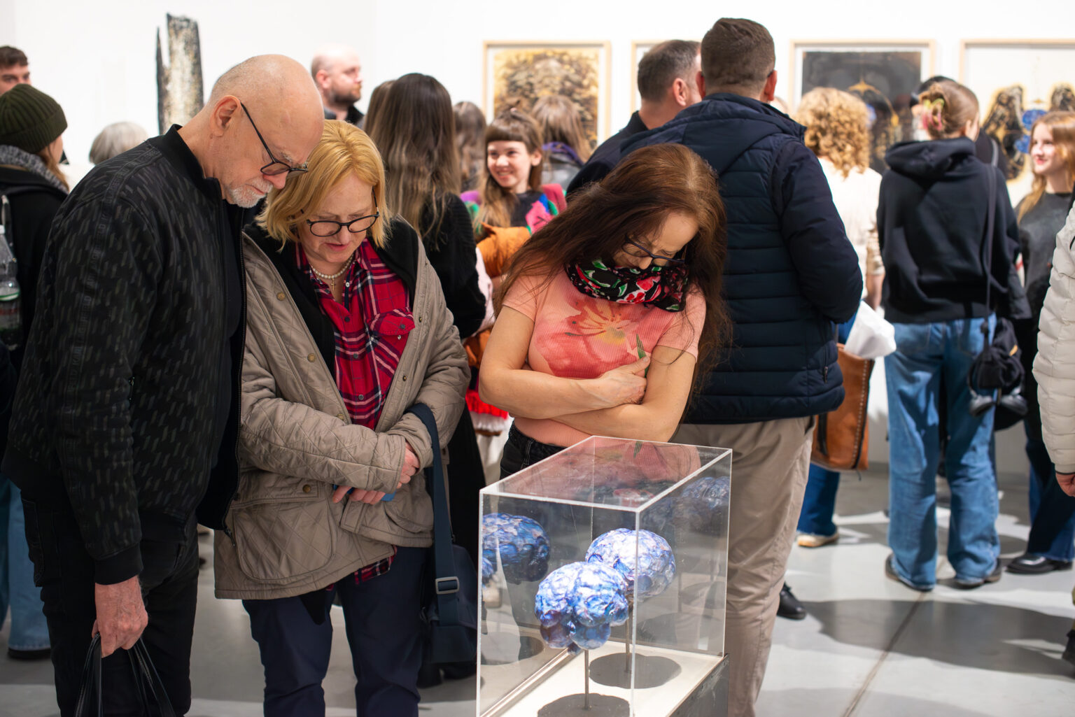 trzy osoby przyglądają się obiektom w gablocie, widok wystawy w tle