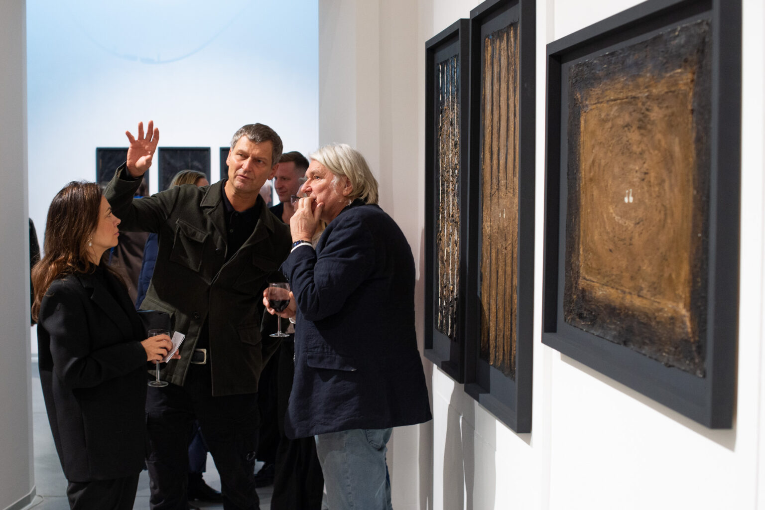 dwaj mężczyźni rozmawiają (eden gestykuluje)na tle duzych obrazów w złotych barwach