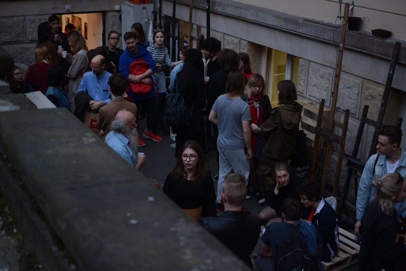 fotografia. Widok z góry grupy ludzi stojących i siedzących przed wejściem do galerii.