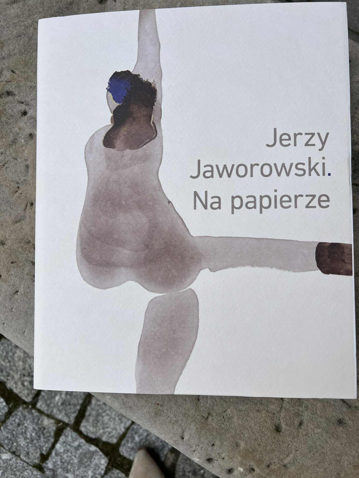 Okładka albumu "Jerzy Jaworowski. Na papierze". Abstrakcyjna, akwarelowa ilustracja figury ludzkiej w odcieniach brązu i granatu. zdj. Agata Rachwał