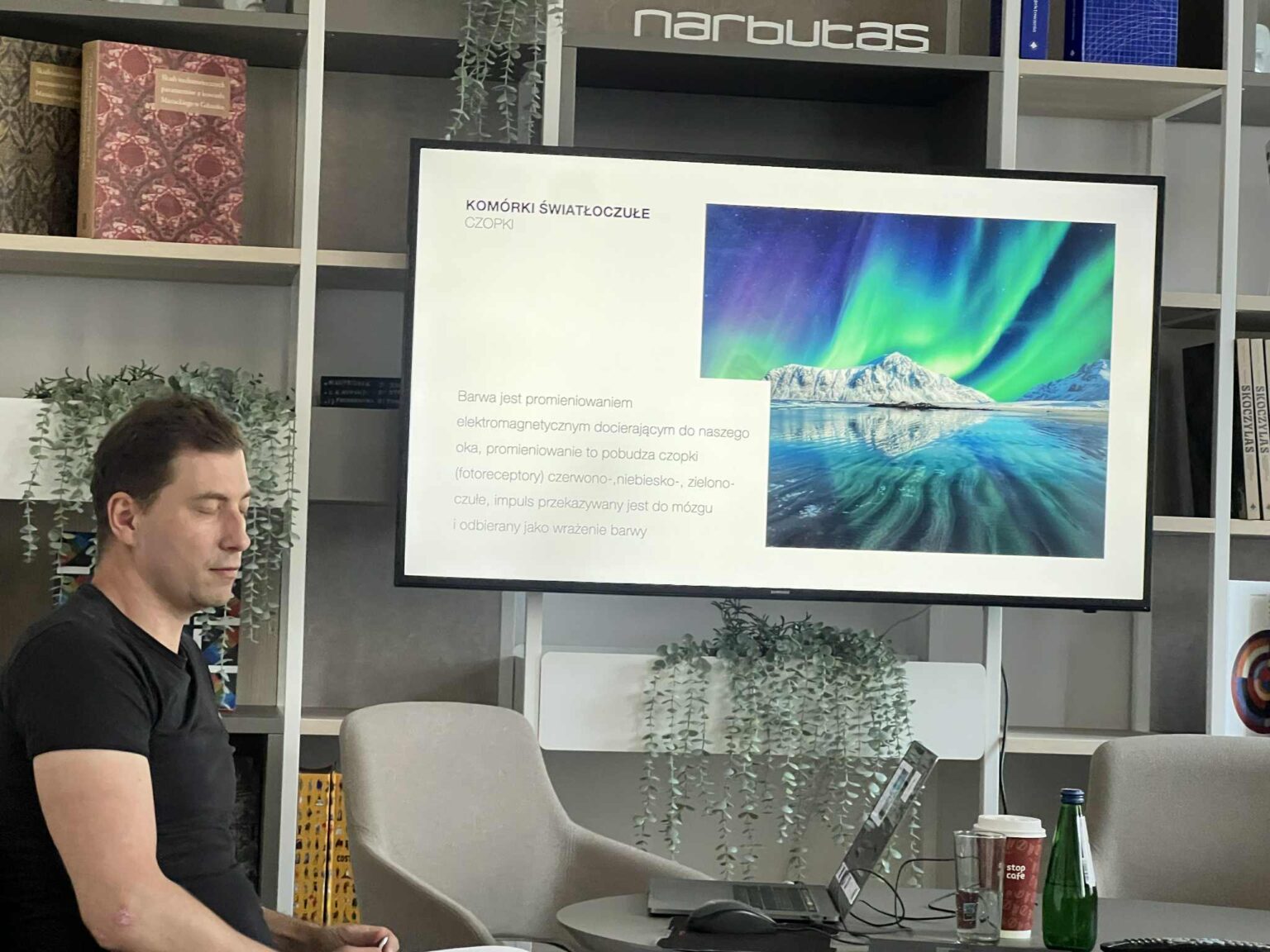Mężczyzna siedzący obok ekranu z prezentacją o komórkach światłoczułych i kolorze. Na slajdzie zdjęcie zorzy polarnej na tle gór. zdj.Agata Rachwał