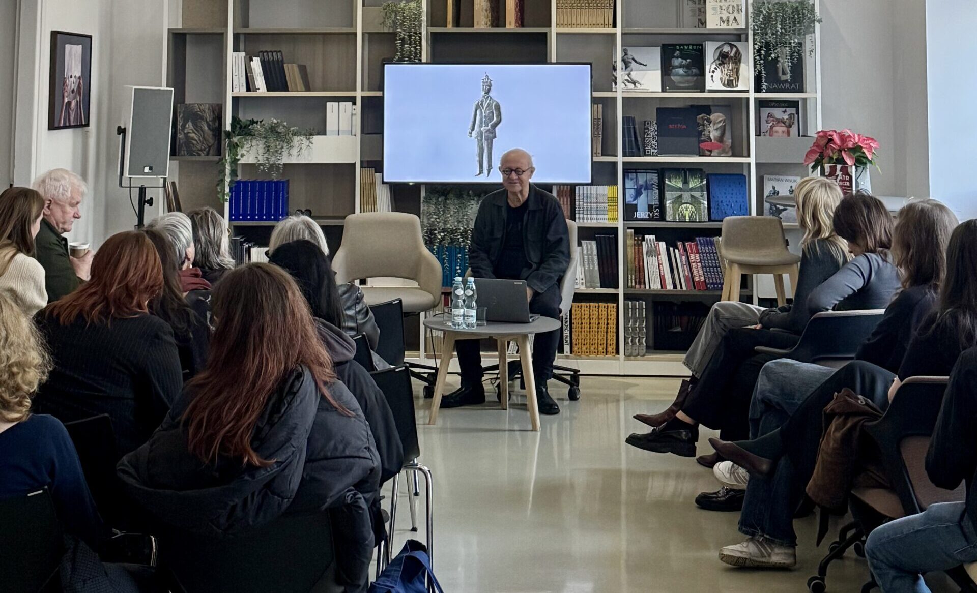 Na tle dużej półki z książkami stoi Maciej Buszewicz, przemawiający do widowni. zdj.Anita Lewandowska